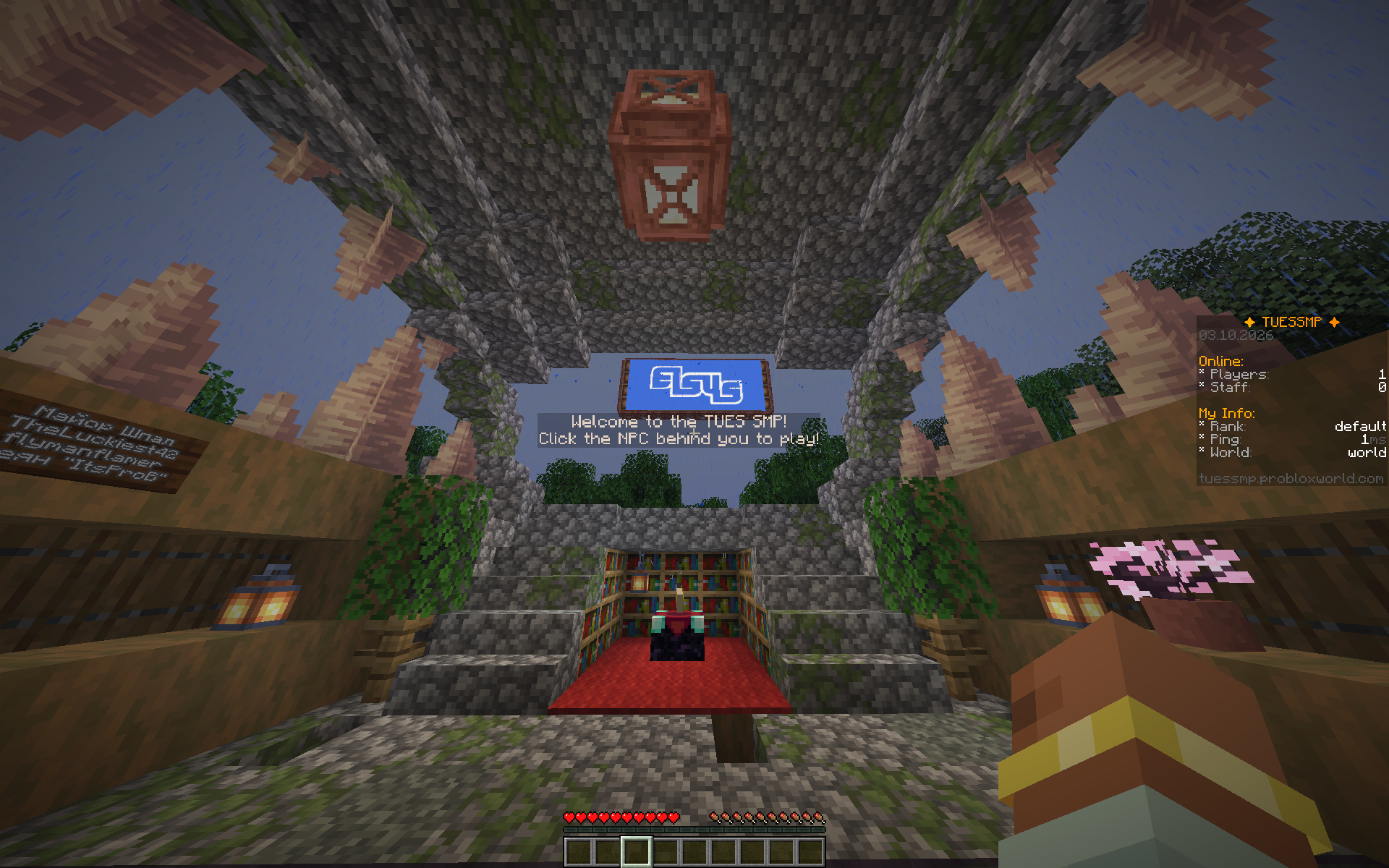 A first-person screenshot of the TUES SMP spawn, showing the stone arch, welcome sign, and enchanting area